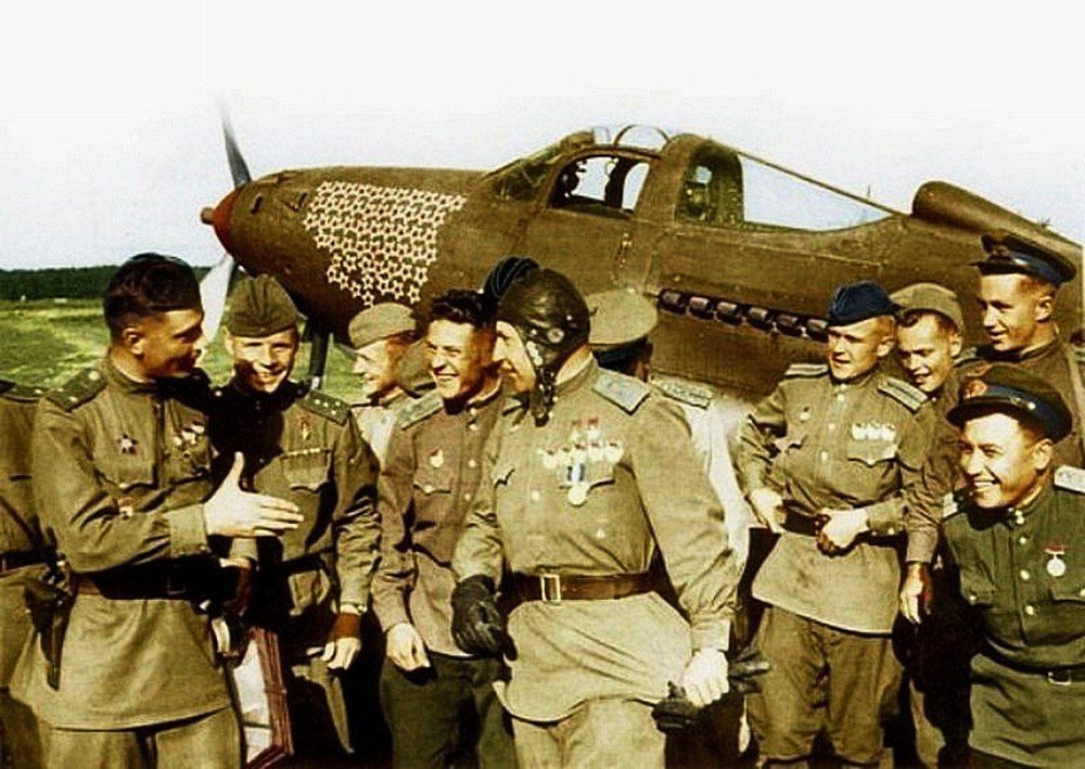 А.И. Покрышкин (в центре) со своими боевыми побратимами. На заднем плане его самолёт «Аэрокобра» со звёздами – знаками побед лётчика-аса